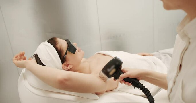 Beautician removes hair on beautiful female armpit using a laser. Hardware removal of hair on the legs in a beauty salon. Laser hair removal of armpit in modern cosmetology clinic.