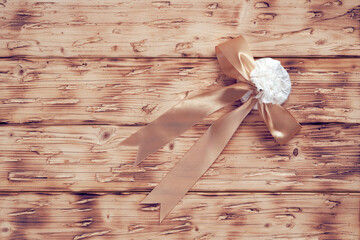 A small round box wrapped in white paper and tied with a gold ribbon lies on a wooden table. A beautiful handmade gift with a big bow for dear people.