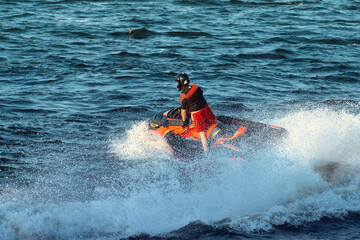 A man rides a jet ski on the sea. The driver of a watercraft performs tricks, splashing water to the sides.