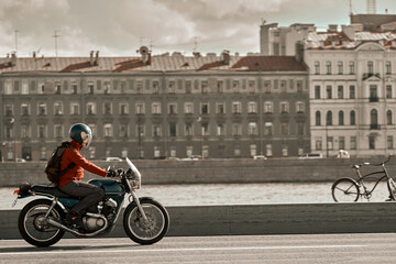 A man rides a modern classic motorcycle in a European city, next to the river. Biker travels the country on a stylish standard motorbike.