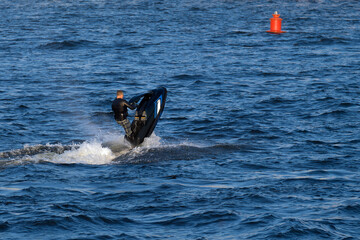 An athlete on a jet ski performs stunts in the sea. Rider man standing floats on aquatic motorcycle jumping on water.