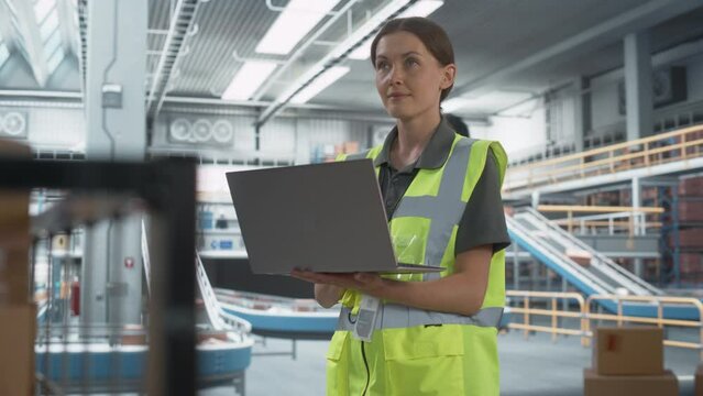 Sortation Fullfilment Center: Female Stocking Associate Uses Laptop. Transportation Warehouse Facility with Conveyor Loading Product Boxes. Employees Carrying Packages To Deliver To Customers.