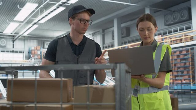 Caucasian Female Logistics Specialist And Male Stocking Associate Talking And Using Laptop In Warehouse Facility With Conveyor Belt. Man Using Barcode Reader To Check Inventory In Distribution Center.