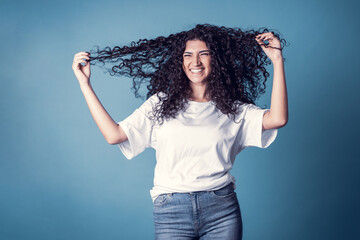Shot of happy confident curly woman with toothy smile, wears casual basic solid white t-shirt,...