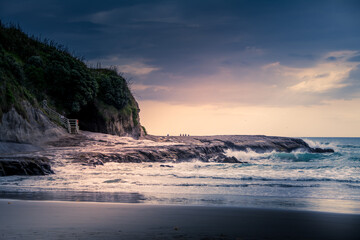 Sunset at Muriwai beach with waves splashing against the rocks and fishermen silhouettes in the...
