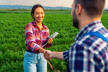 The Caucasian farmer and the Chinese agronomist in a carrot field have closed a deal. They shake...