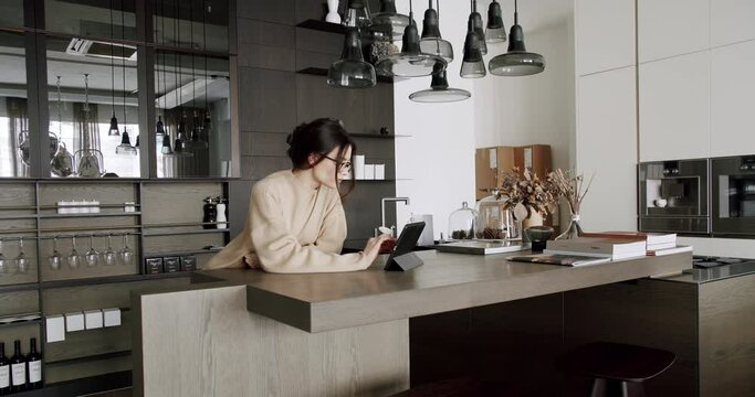 Beautiful woman at home using digital tablet in modern kitchen room and loft apartment. ooking digital tablet for follow news, work and social media online in loft kitchen at home
