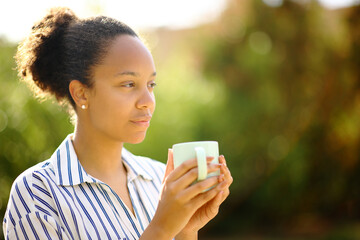 Relaxed black woman holding coffee mug looks away