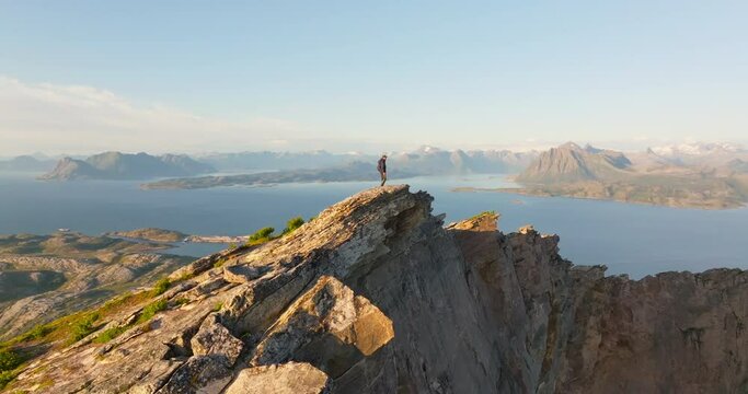 Climber on arctic mountain summit with panorama midnight sun view; drone