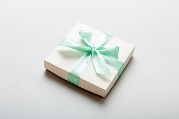 wrapped Christmas or other holiday handmade present in white paper with green ribbon on colored background. Present box, decoration of gift on colored table, top view with copy space