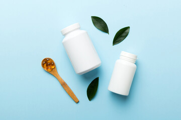 Omega-3 capsules lie in white bottle on a table with green leaves background. Fish oil tablets....