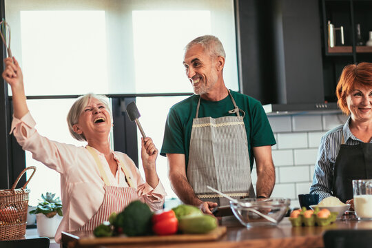 Group of senior friends at dinner party at home, cooking. - Powered by Adobe