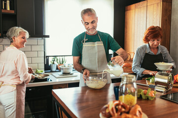 Group of senior friends at dinner party at home, cooking.