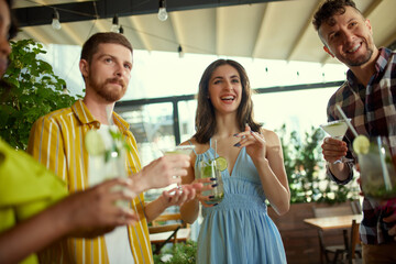 Cheerful, positive young people, friends meeting together at cafe to drink, talk and spend time together. Conversation. Concept of friendship, meeting, fun, communication, alcohol drinks