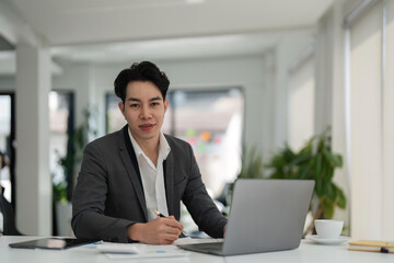 Young Asian business man executive working on financial strategy on laptop at corporate office. Professional businessman manager using computer technology sitting at table