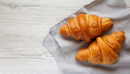 Freshly baked croissants on cloth on white wooden table, overhead view. From above, top view, flat lay. Close-up.