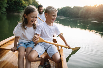 Lauging boy and girl paddling canoe with their father