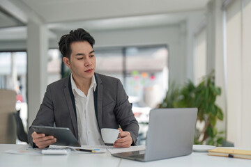 Focused young adult businessman asian sitting at desk making sure his company is earning enough money financial planning concept