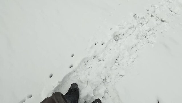 A climber taps an ice pick on a shoe in climbing cats to shake off the stuck snow. A first-person view of the legs down. Climbing Belukha. Snow trail in the mountains. Beautiful nature of Altai