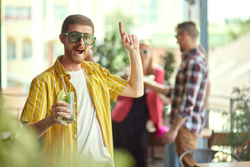 Focus on cheerful man in colorful clothes and sunglasses meeting with friends in cafe. Blurred...