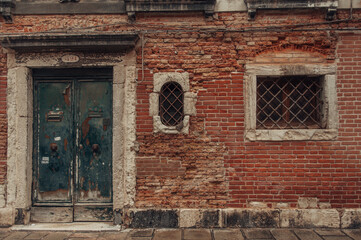 Fototapeta na wymiar An aged building in Venice with weathered facade, barred windows, damaged brickwork, and a worn-out door.