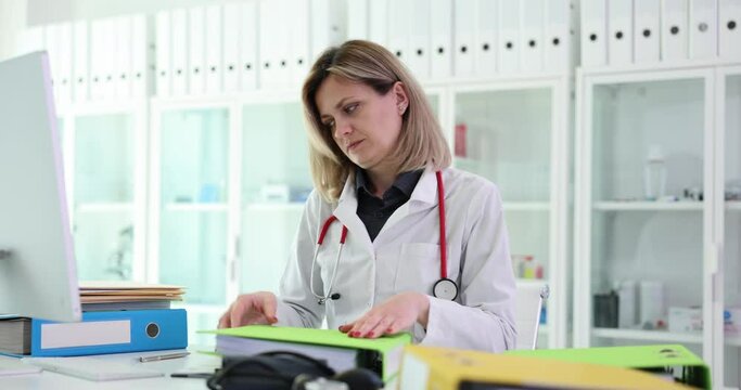 Female medic inserts paper documents into folder for patient data storage. Concept of sorting and workflow of specialist at workplace. Medical profession