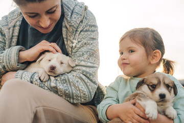 Cute little girl and her mother hugging dog puppies outdoors. Friendship and care concept