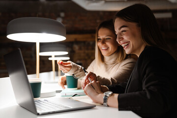 Two cheerful woman working on laptop while sitting in office