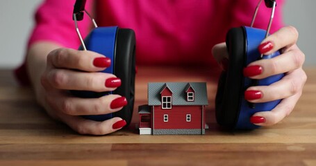 Female person puts headphones over small toy house sitting at wooden table. Home protection concept. Home soundproofing for comfortable life
