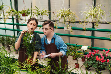 Man writing down notes in clipboard while woman florist teaching him to handle with flowers in...