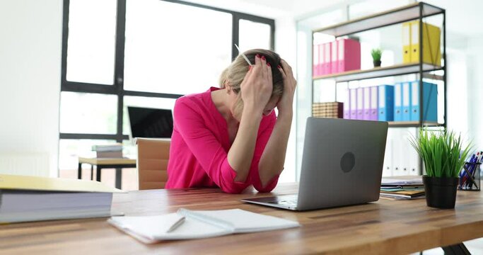 Young woman doomed grabs head holding bank card in hand against laptop. Lady in office realizes being deceived on Internet. Internet fraud concept