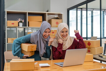 Two women muslim look at online product sales data on laptops and show joy