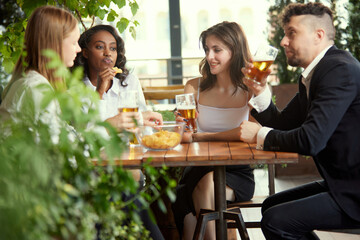 Happy, positive, smiling young people, office workers, colleagues meeting in cafe, pub after work to drink beer, talk and relax. Concept of leisure time, business, communication, fun, alcohol drink