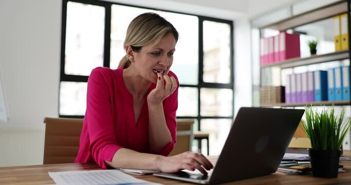 Worrying young employee waits for result of interview with new boss. Lady bites nails in excitement while sits at laptop on table. Bad habit concept
