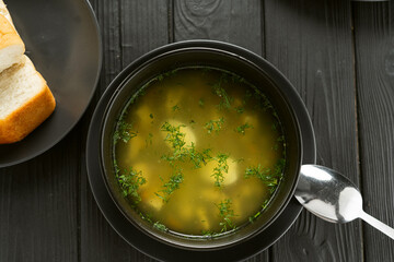 Chicken broth with vegetables in a black bowl. Dark wooden background. View from above.