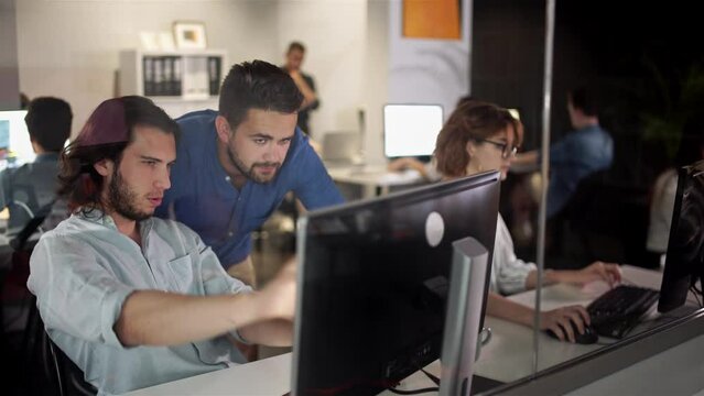 Coworkers looking at a computer and talking about work. Team of colleagues brainstorming together while working on the computer. Men colleagues discuss online project look at pc screen