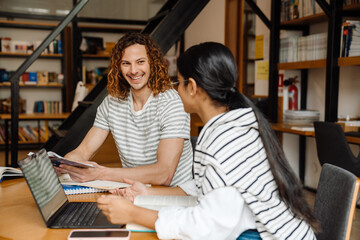 Two multiethnic students preparing for exams together while sitting in library