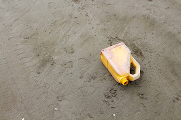 An old, yellow bottle discarded on the beach sand, causing environmental pollution.