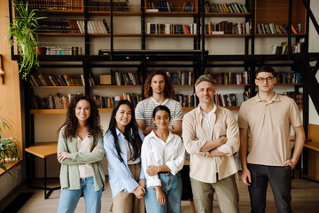 Group of students and adult male teacher smiling at camera while standing in library