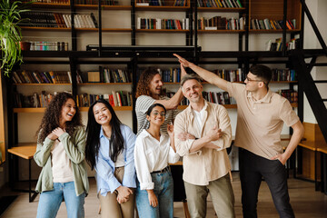 Group of students and adult male teacher smiling at camera while standing in library