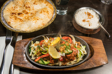 A steaming hot chicken sizzlar in an Indian restaurant with a nnan bread.