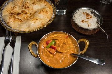 A chicken curry in an indian restaurant with rice and Nan bread.