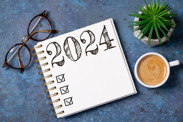 New year resolutions 2024 on desk. 2024 goals list with notebook, coffee cup, plant on wooden...