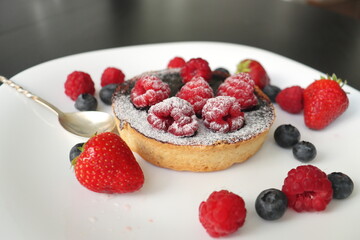 cream cake with raspberries and blueberries and small macaroons served on a large white plate