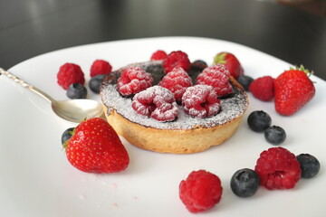 cream cake with raspberries and blueberries and small macaroons served on a large white plate