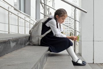 Junior schoolgirl sits with sad expression. Girl with long braids afraid to attend school and see...