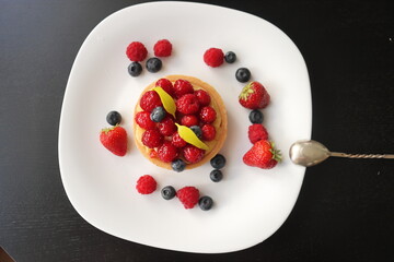 cream cake with raspberries and blueberries and small macaroons served on a large white plate