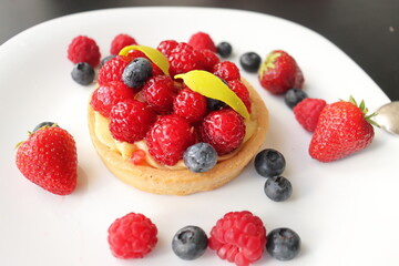 cream cake with raspberries and blueberries and small macaroons served on a large white plate