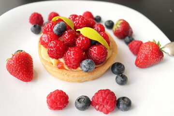 cream cake with raspberries and blueberries and small macaroons served on a large white plate