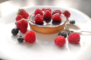 cream cake with raspberries and blueberries and small macaroons served on a large white plate